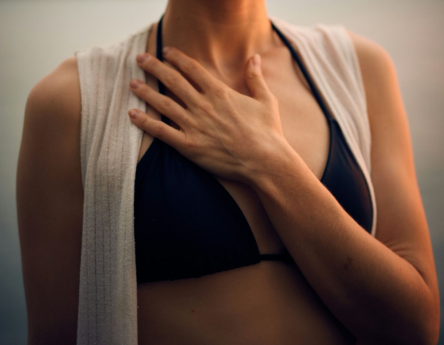 Person wearing a black bikini with a towel draped over their shoulder against a neutral background