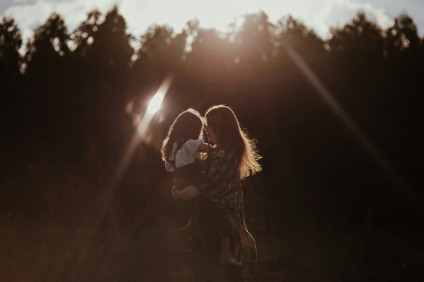 A woman embracing her daughter in a field with a sunflare effect